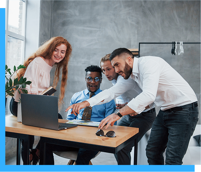 Four colleagues working together with a laptop on a wooden desk in a modern office.