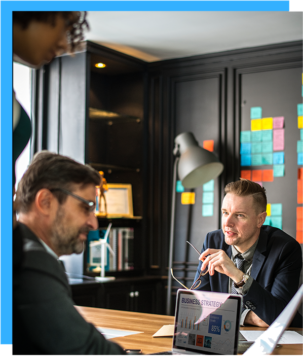 Two professionals in a meeting with sticky notes and a laptop displaying graphs on desk.